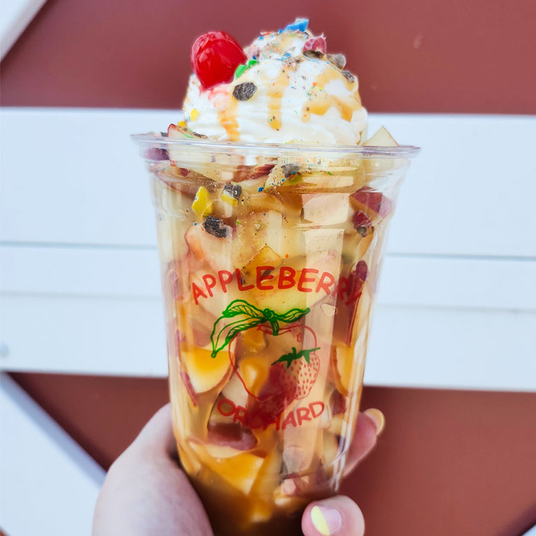 A Caramel Apple Frenzy dessert from Appleberry Orchard featuring fresh apples, caramel, whipped topping, candy crumble, and a cherry.